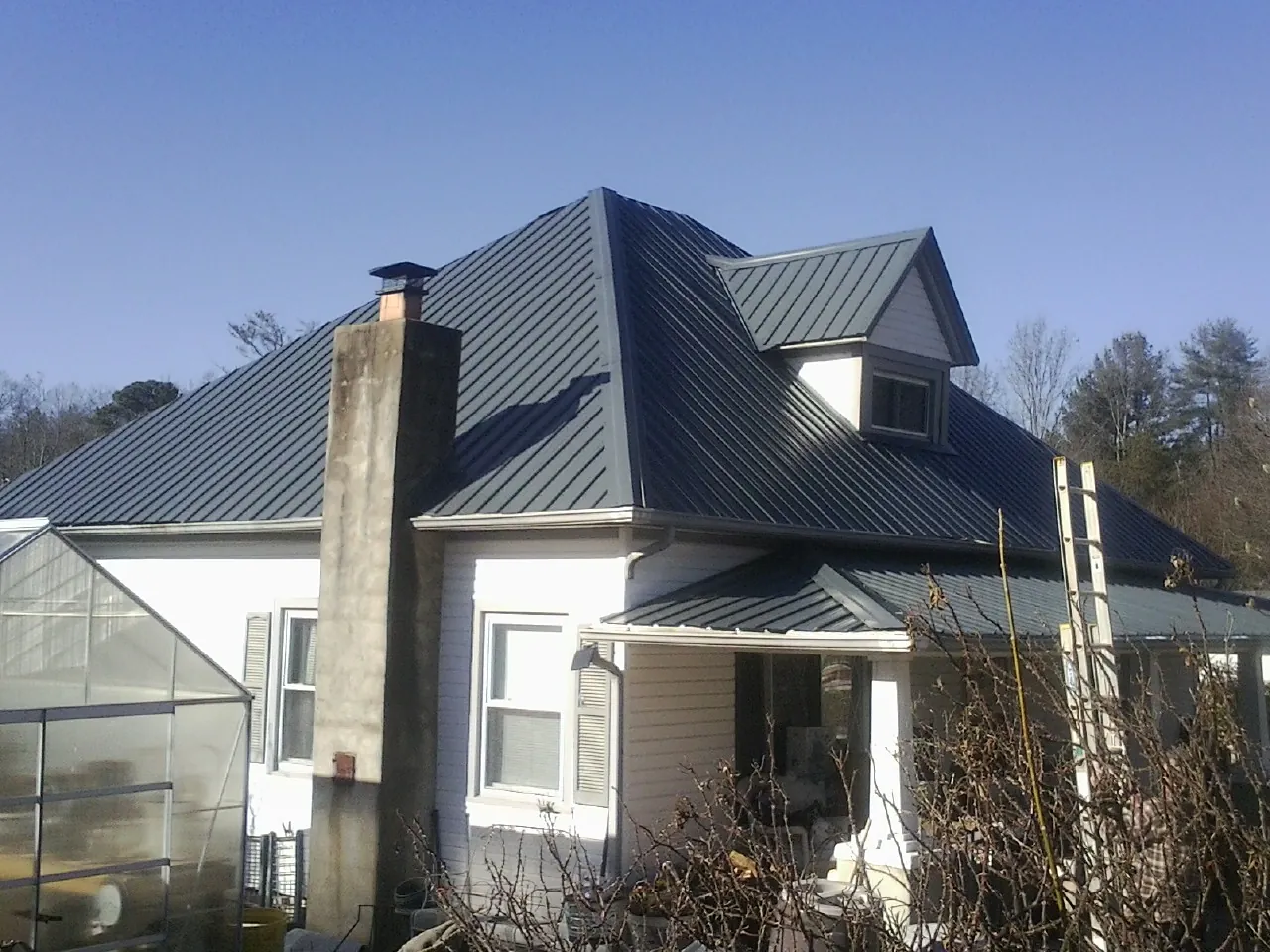 Dark blue standing seam metal roof on a white farmhouse with dormer — Slate & Tile Roof Repair by Roofing Brothers in Baden