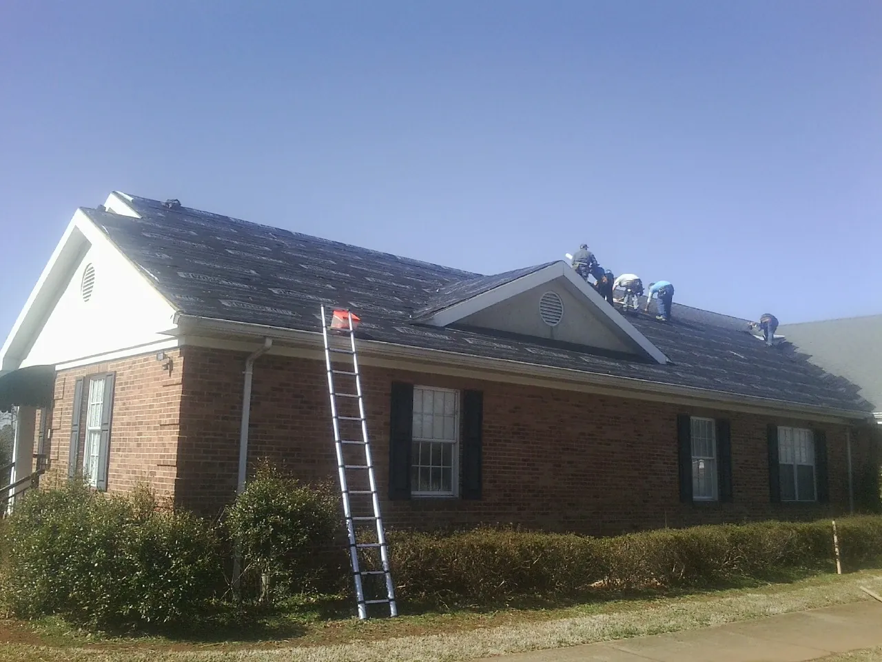 Crew tearing shingles off a brick ranch roof with a ladder set — Emergency Roof Repair work by our crew in Baden