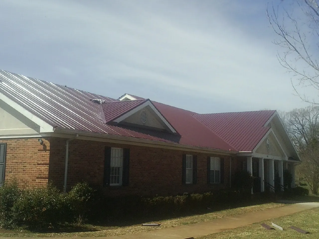 Red metal roof with gabled entries on a long brick building, from a Hail Damage Roof Repair job in Baden