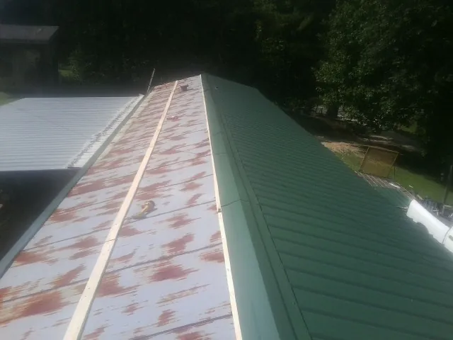 Old rusted panels beside newly installed green metal roofing — Wind Damage Roof Repair by Roofing Brothers in Baden